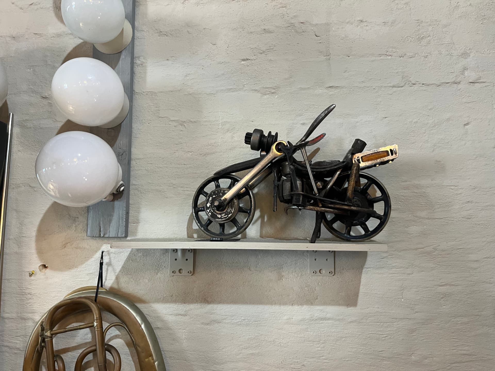 Skulptur av motorcykel i metall bredvid vägglampor i opalglas